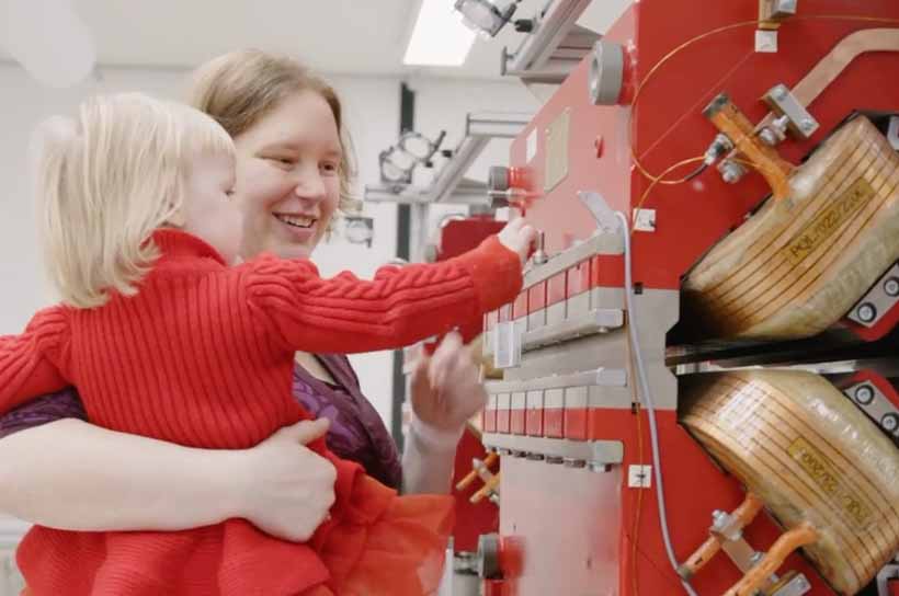 In der Testwerkstatt hält Ingenieurin Jana Barker ihre Tochter auf dem Arm. Gemeinsam betrachten sie zur Vermessung aufgebaute Magnete.