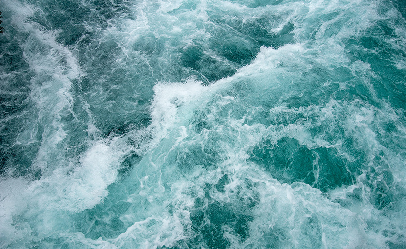 Die Kraft des Wassers wird versinnbildlicht durch die schäumenden Wellen der Meeresoberfläche.