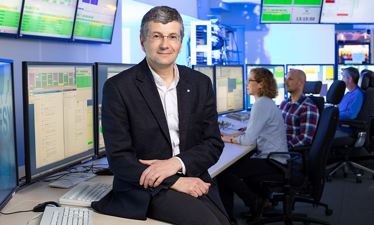 A male person sits on a table in front of monitors